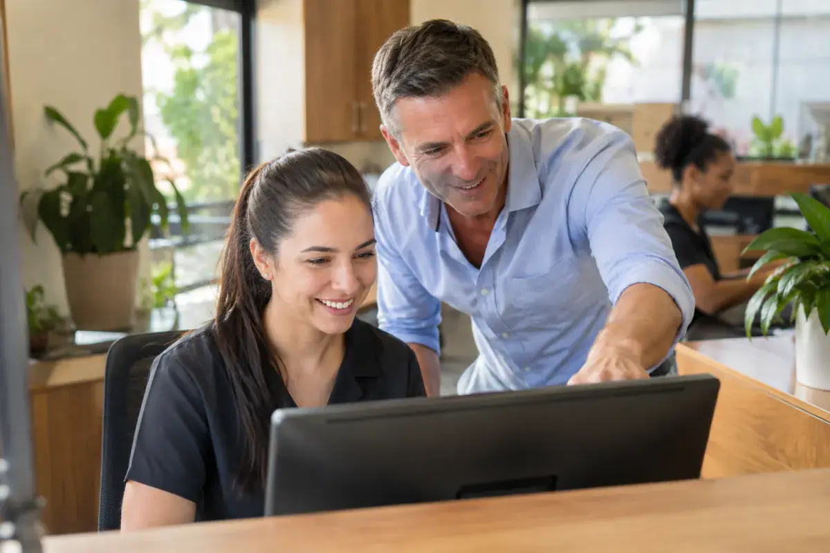 A business owner and his receptionist smiling at new enquiries on the front-desk computer